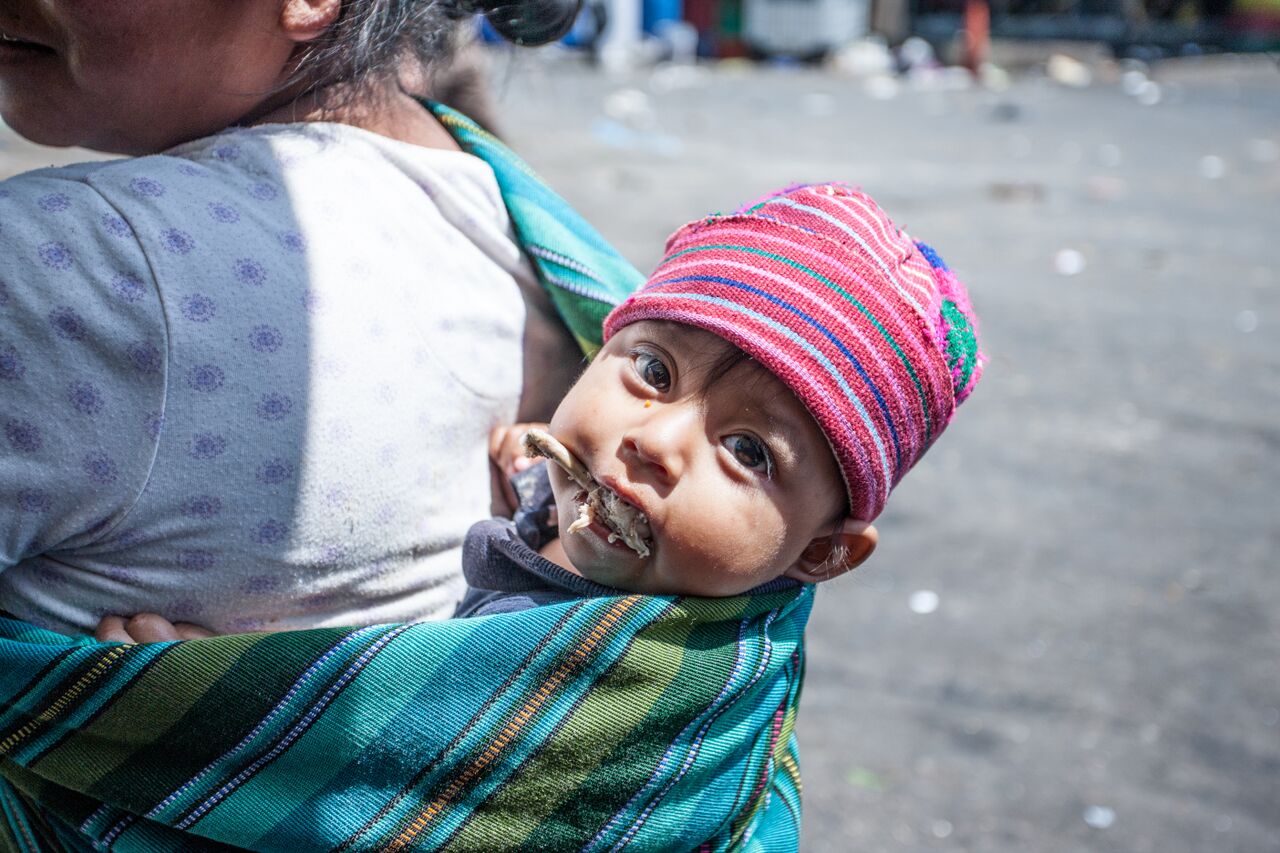 Guatemalan baby on mothers back eating a chicken bone