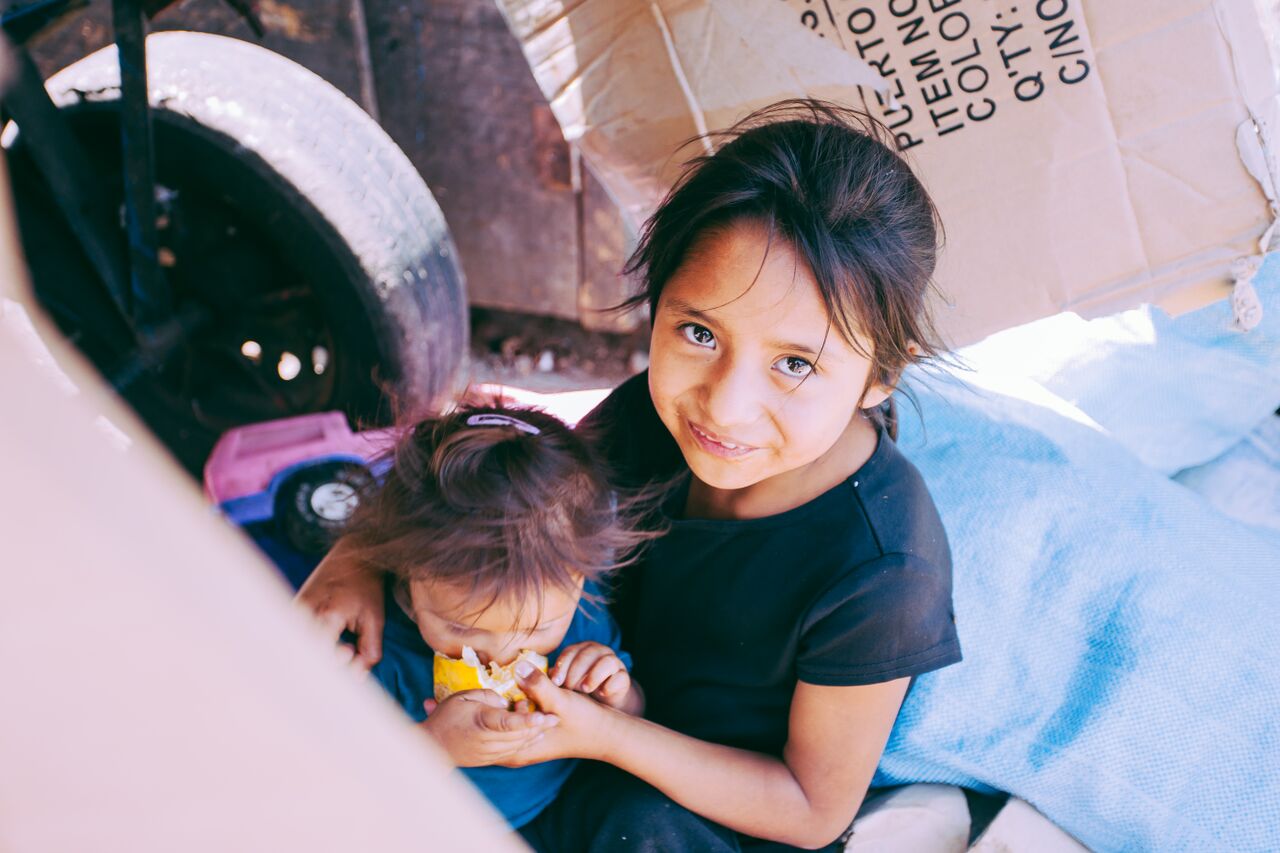 Big sister feeding little sister outside city dump